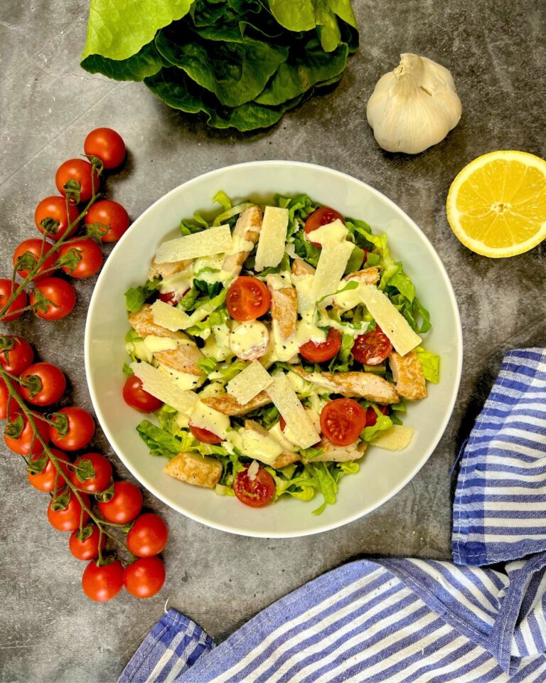 Eine Schüssel gesunder Caesar Salat. Gefüllt mit gegrilltem Hähnchen, Cherrytomaten, Croûtons und Parmesanspänen.