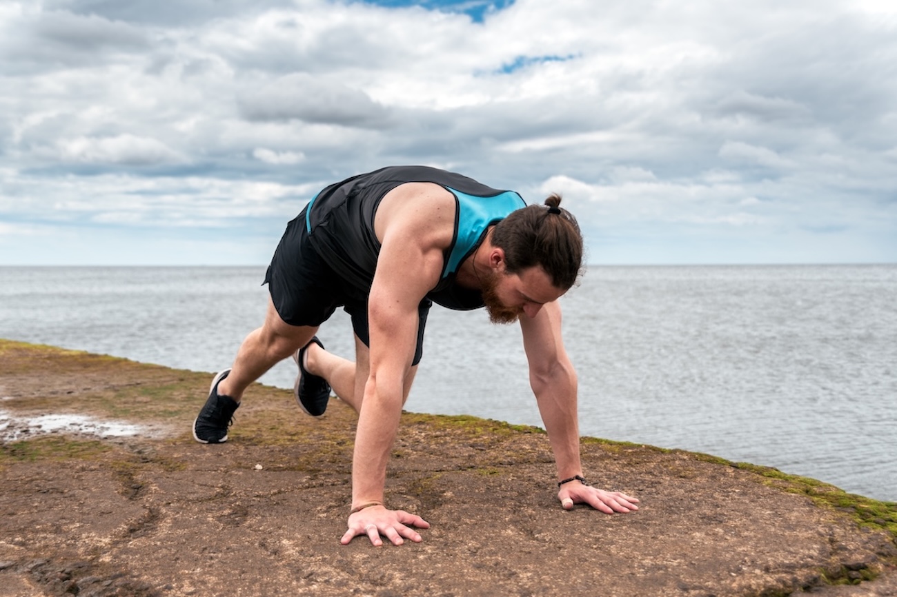Junger man macht MountainClimbers in der naehe der Kueste Ein bärtiger Mann mit Dutt macht Mountain Climbers in der nähe der Küste