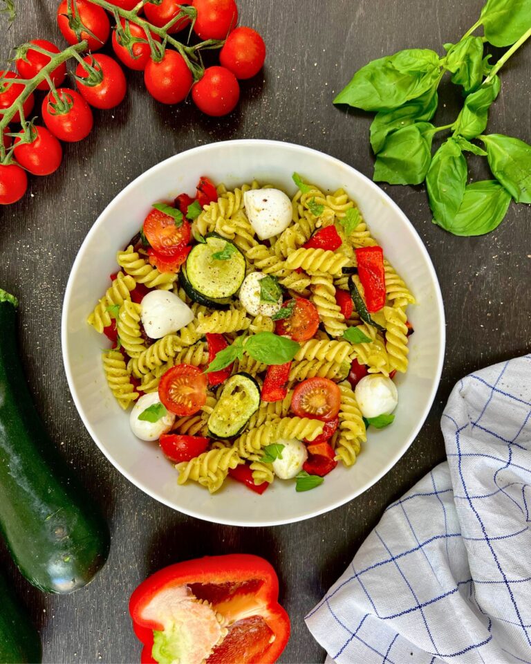 Eine leckere Pesto-Pasta Bowl, bestehend aus Fusilli-Nudeln, Zucchinischeiben, Kirschtomaten, Mozzarellakugeln und Basilikumblättern.