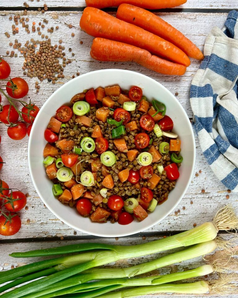 Eine Schüssel veganer Linsensalat mit Cherrytomaten, Karotten, Frühlingszwiebeln und Kräutern.